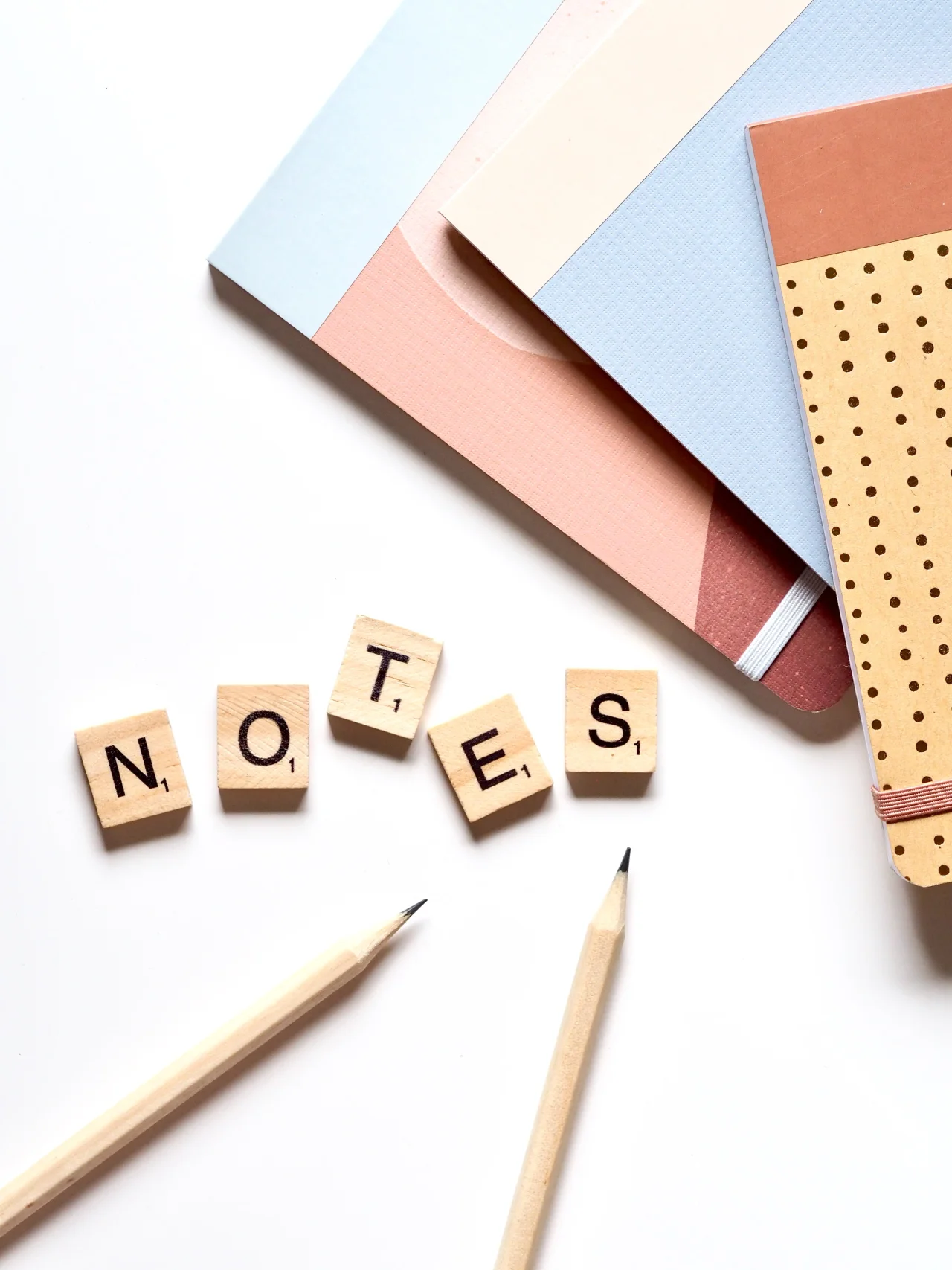 Carnets et crayons avec lettres en bois formant le mot notes posés sur une table